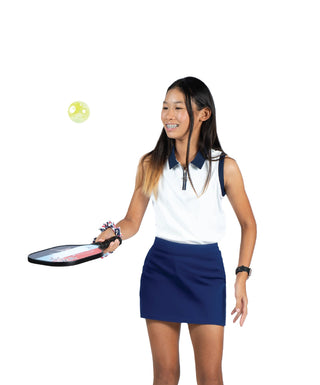 Birdie Vibes Sleeveless Polo White / Navy — Girls' Golf Polo, front view, full length on model, holding a paddle